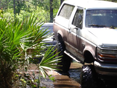 1989 Ford Bronco - This 1989 Ford Bronco appears to be stuck in a muddy area, with another vehicle partially visible behind it.