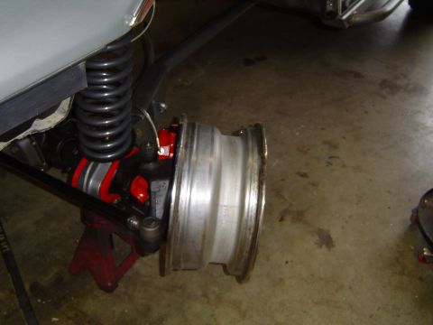 1989 Ford Bronco - Close-up of a vehicle's rear axle assembly, supported by a red jack stand, with the wheel removed and the coil spring in view.