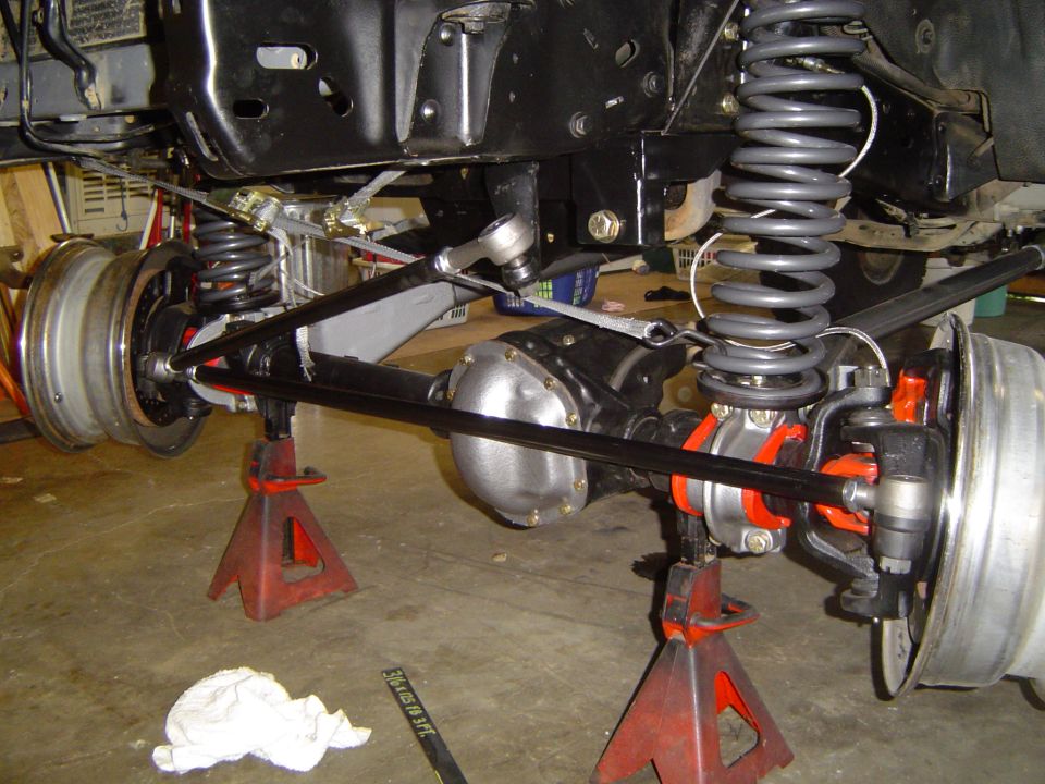1989 Ford Bronco front axle and suspension on jack stands, showing red suspension components and silver differential