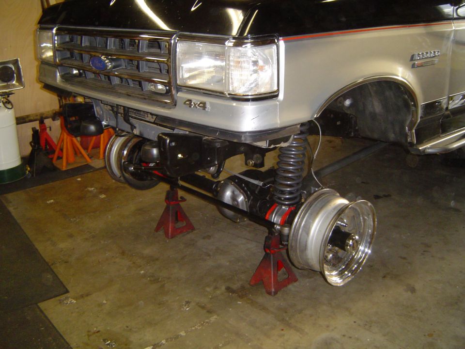 Front of two-tone Ford Bronco on jack stands with axle and wheel removed in garage