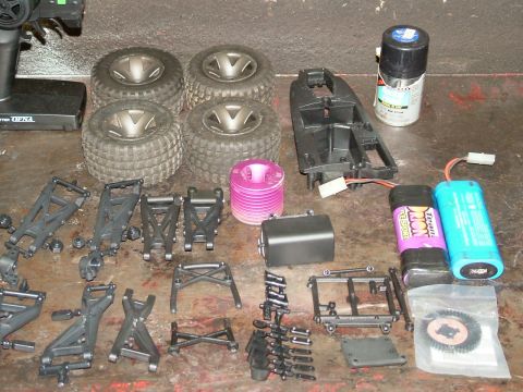 1994 Ford Bronco - Various parts for an RC car, including tires, suspension components, batteries, and a remote control, are spread out on a surface.