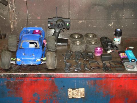 1994 Ford Bronco - A blue remote control monster truck is displayed with its various parts, including extra wheels, suspension components, batteries, and a co…