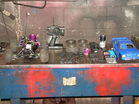 1994 Ford Bronco - A collection of remote control car parts, including a chassis, tires, and a blue body, are laid out on a workbench.