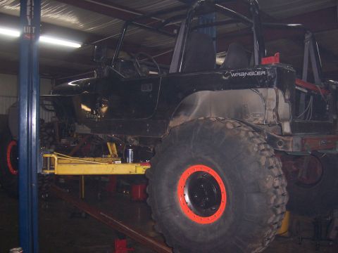 1999 Jeep TJ - A black 1999 Jeep TJ Wrangler is shown on a lift, equipped with oversized off-road tires and a roll cage.