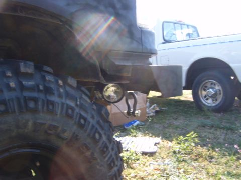 1988 Ford Bronco - A large off-road tire and tow hitch are visible on a vehicle, with a white pickup truck in the background.