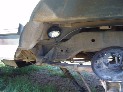 1988 Ford Bronco - A rock light is mounted to the rusty frame of a vehicle, with the brake drum visible in the background.