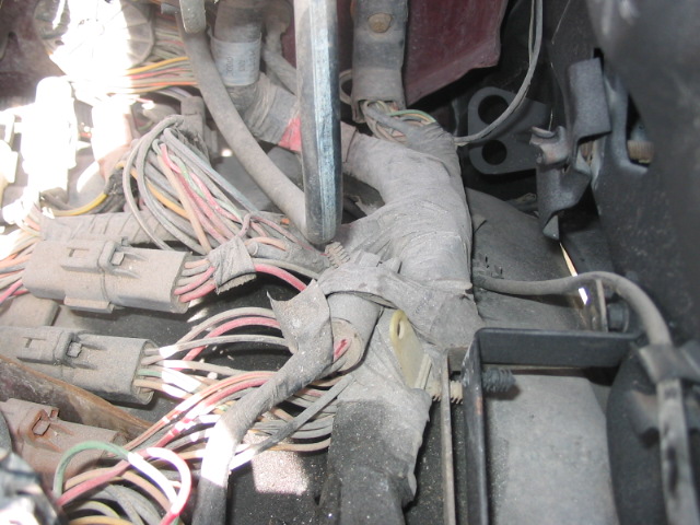 Close-up of a dusty, tangled vehicle wiring harness with multiple connectors and taped bundles