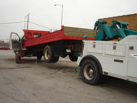 1992 Ford Bronco - A tow truck is towing a red flatbed truck. A red car is in the background.