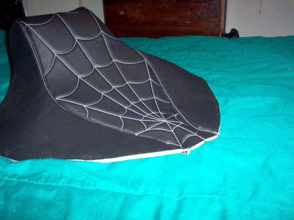 Black vinyl seat with white spiderweb stitching lying on a teal blanket