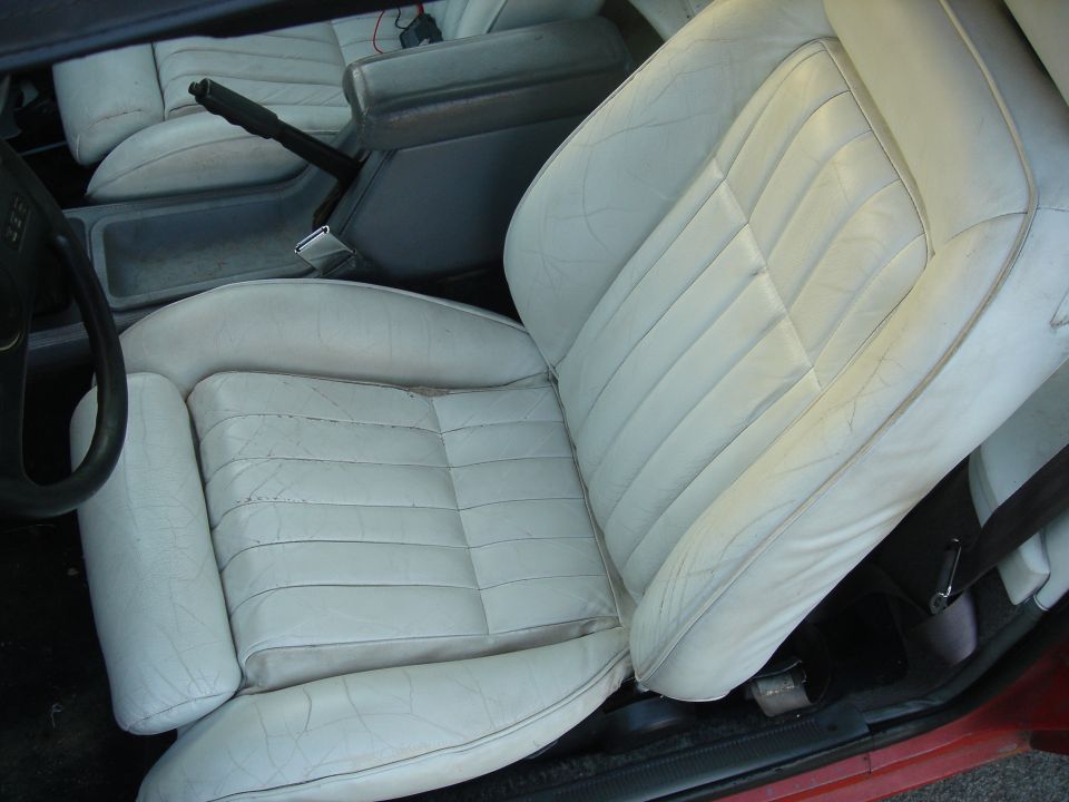 Car interior with white leather seats and a black steering wheel. A red exterior is visible