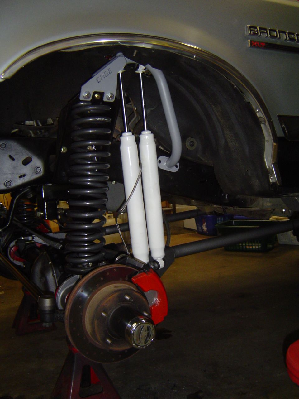 Solid front axle swap on a white Bronco: coil spring, dual white shocks, red caliper, locking hub