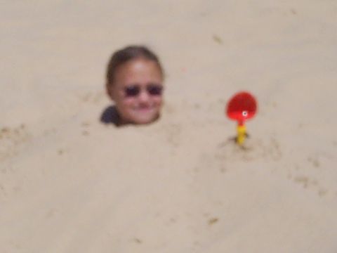 1985 Ford Bronco - A child is buried in the sand at the beach with a red toy nearby.