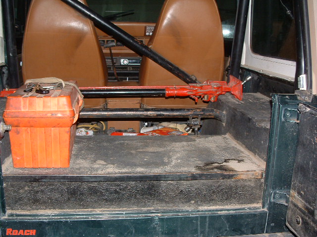 Green Jeep YJ interior, rear cargo area with orange toolbox and red Hi-Lift jack. Brown seats visible