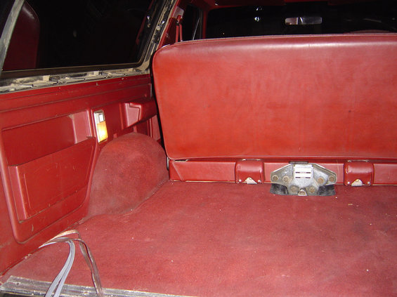 Red carpeted interior cargo area of a 1978 Ford Bronco with a folded rear seat and a visible latch mechanism