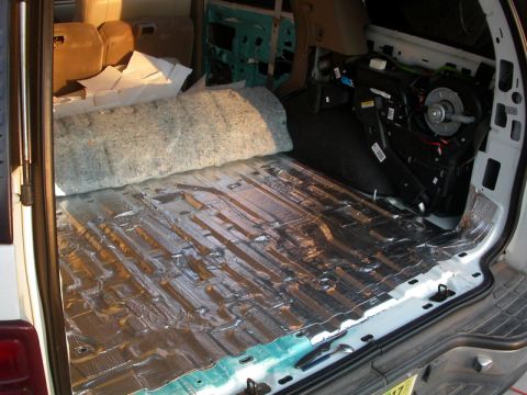 1978 Ford Bronco - Sound deadening material being installed in the cargo area of a vehicle, covering the floor with foil insulation and foam padding.