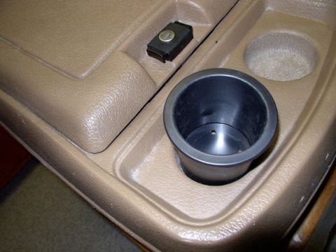 1978 Ford Bronco - Close-up of a vehicle's interior center console, a cup holder and a small black latch mechanism.