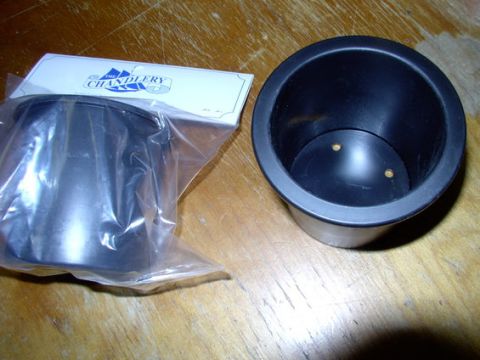 1978 Ford Bronco - A black plastic cup holder and a metal cup holder in packaging are displayed on a wooden surface.