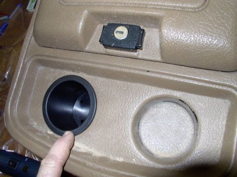 1978 Ford Bronco - Close-up of a vehicle's tan center console, showing two cup holders and a small lockable compartment.