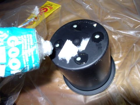 1978 Ford Bronco - A black plastic part, possibly from a vehicle's center console, has glue being applied to it.