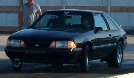 1989 Ford Mustang - A black 1989 Ford Mustang is shown on a race track with a person standing in the background.