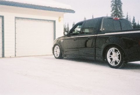 2003 Ford F-150 - A black 2003 Ford F-150 pickup truck sits in a snowy landscape beside a white garage door.