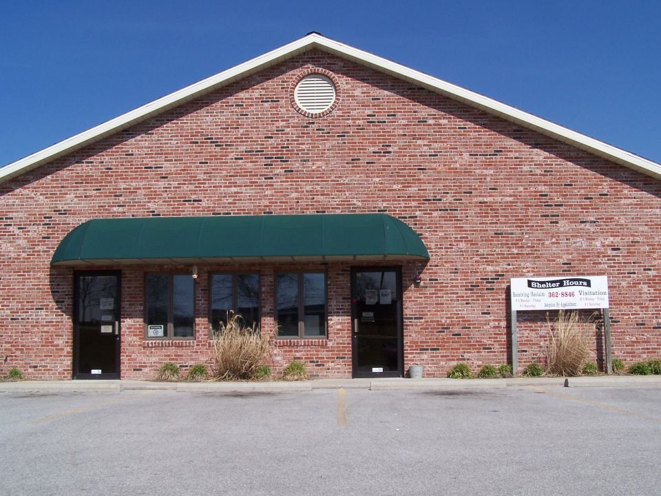 Brick building with green awning over two doors and windows. Signage visible