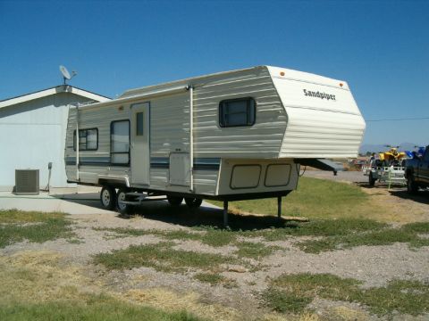 1985 Ford Bronco - A Sandpiper brand camper is parked outside a residence under a clear blue sky.
