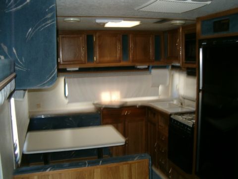 1985 Ford Bronco - The interior of a trailer features a dinette, a corner kitchen with a sink and stove, and a black refrigerator.