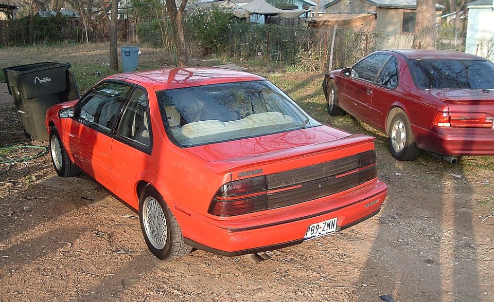 Red Chevrolet Beretta coupe rear three-quarter view in dirt yard