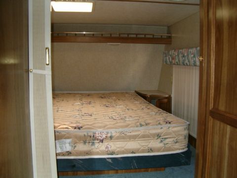 1985 Ford Bronco - Interior view of a camper or RV bedroom, a bed with a floral comforter and wood paneling.