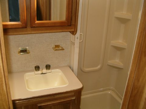 1985 Ford Bronco - This image shows the interior of a bathroom, a sink, shower stall, and wooden cabinets.