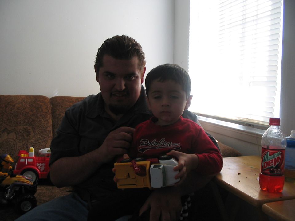 Father and son on a couch with toys, including a red toy fire truck and a yellow toy
