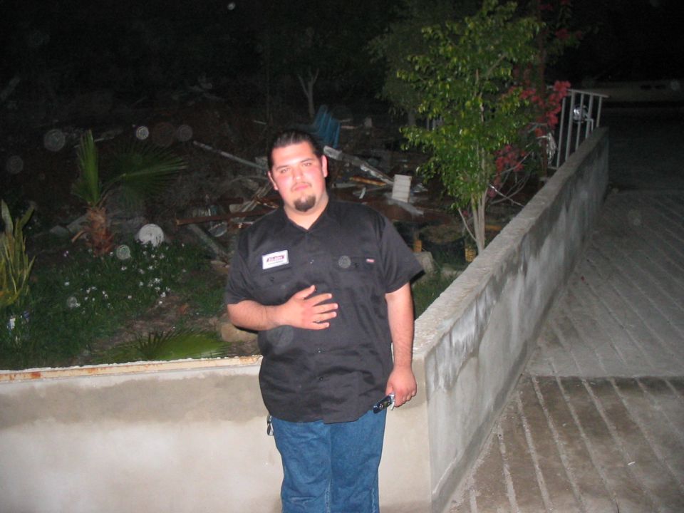 Man in black work shirt and blue jeans standing outdoors at night