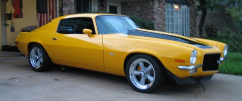 1972 Chevrolet Camaro - A yellow 1970 Chevrolet Camaro with black racing stripes is parked in front of a brick house.
