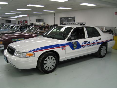 1991 Ford LTD Crown Victoria - Front three-quarter view of a white Ford police cruiser marked 'POLICE MARLBOROUGH' with a roof light bar in a showroom.
