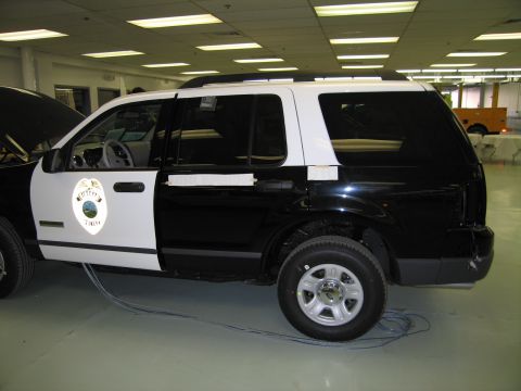 1991 Ford LTD Crown Victoria - Side-rear view of a black-and-white police SUV with a circular door seal and silver wheels, parked in a showroom.