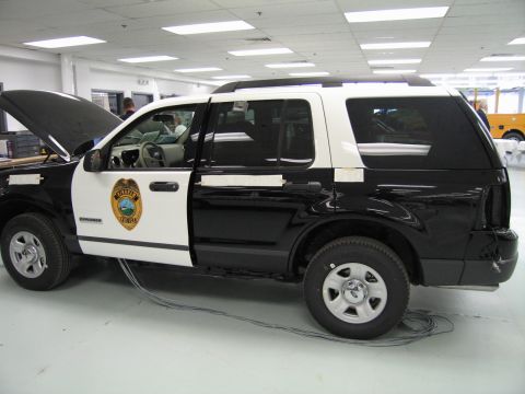 1991 Ford LTD Crown Victoria - black-and-white police-style SUV with its hood raised and a circular door emblem, displayed inside a showroom.