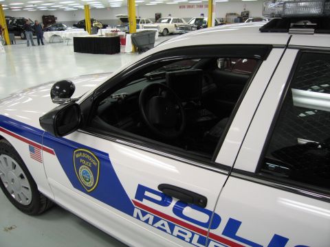 1991 Ford LTD Crown Victoria - Close-up of a white 'POLICE MARLBOROUGH' cruiser's front door, side mirror and window with people visible in background.