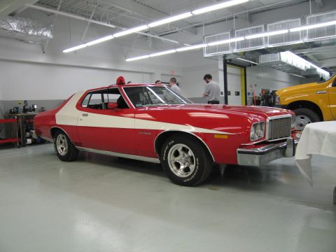 1991 Ford LTD Crown Victoria - red two-door coupe with a wide white vector stripe and chrome bumpers parked in a garage, with a yellow truck beside it.