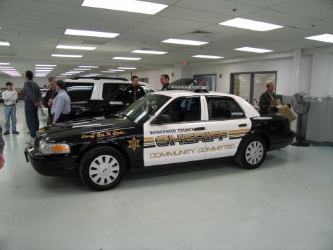 1991 Ford LTD Crown Victoria - black-and-white sedan marked 'WORCESTER COUNTY SHERIFF - COMMUNITY COMMITTED' parked indoors with people standing around it.