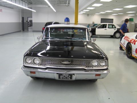 1991 Ford LTD Crown Victoria - Head-on front view of a black 1960s Ford sedan with quad headlights, blue dome light and a license plate reading 85252.