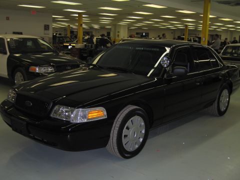 1991 Ford LTD Crown Victoria - Front three-quarter view of a black Ford sedan fitted with a side spotlight and steel wheels, parked on a polished floor.