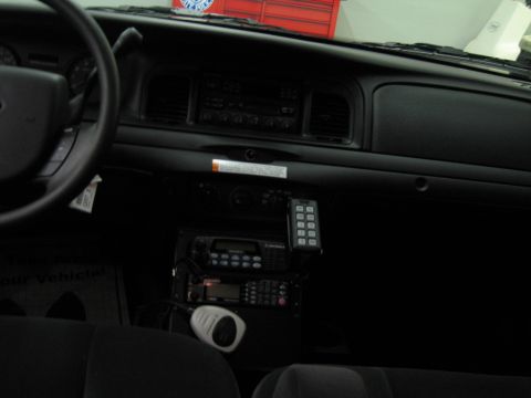 1991 Ford LTD Crown Victoria - Interior dashboard of a Ford vehicle showing a stock radio and floor-mounted police radio control heads with a handset.