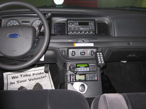 1991 Ford LTD Crown Victoria - Ford vehicle dashboard with center-stack police radio gear, a microphone, and a printed We Take Pride In Your Vehicle sign on the seat.