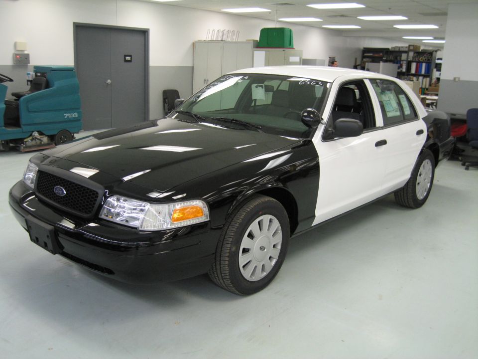 Front three-quarter view of black and white Ford Crown Victoria sedan in a shop
