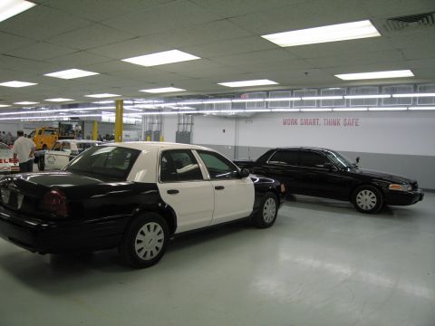 1991 Ford LTD Crown Victoria - black-and-white Ford sedan and a solid black Ford sedan parked side by side in a large workshop with a WORK SMART wall sign.