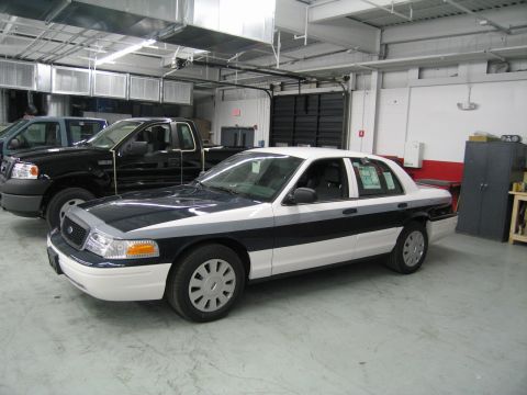 1991 Ford LTD Crown Victoria - Front three-quarter view of a black-and-white Ford sedan parked next to a black pickup truck inside a garage bay.