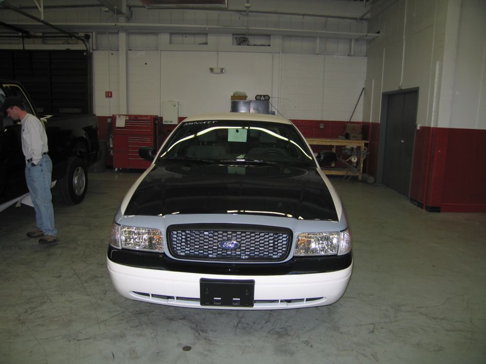 Head-on front view of white Ford sedan with chrome grille and a man standing nearby