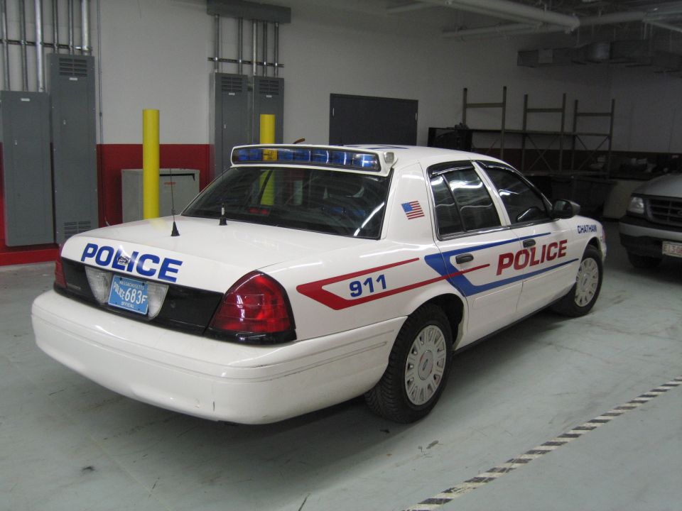 Rear three-quarter view of white Crown Victoria police car with POLICE 911 and US flag decals