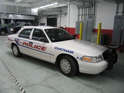 1991 Ford LTD Crown Victoria - Side profile of a white police car lettered POLICE, CHATHAM and unit F-7 with blue striping, parked indoors in a garage bay.